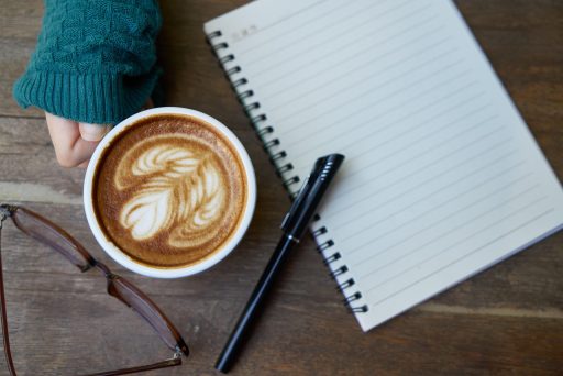 Vrouw schrijft in notitieboekje aan tafel met kop koffie tijdens ochtendrutine