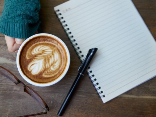 Vrouw schrijft in notitieboekje aan tafel met kop koffie tijdens ochtendrutine